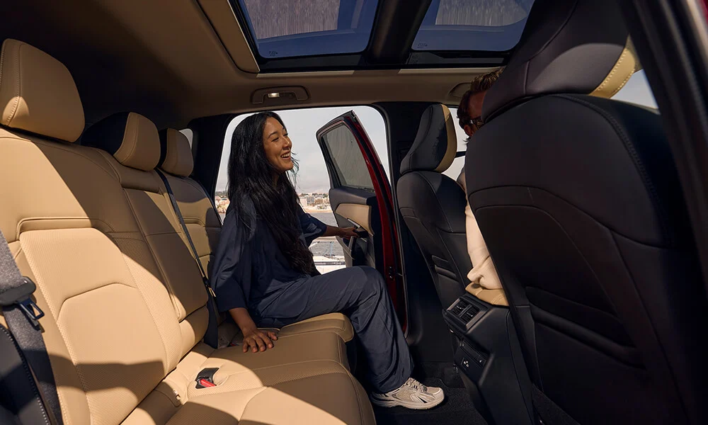 Vue des sièges arrière à partir de la portière côté passager, avec une femme qui entre du côté conducteur.  